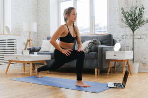 white woman does a runners stretch in black leggings and sports bra in a living room